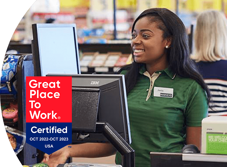 'Great Place to Work - Certified Oct 2022-Oct 2023' - Harveys Supermarket cashier smiling and checking out items
