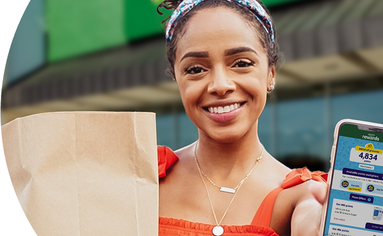 Woman smiling outside of a Harveys Supermarket holding a grocery bag and phone with Harveys app