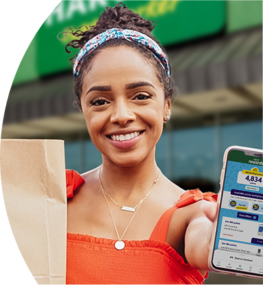 Woman smiling outside of a Harveys Supermarket holding a grocery bag and phone with Harveys app