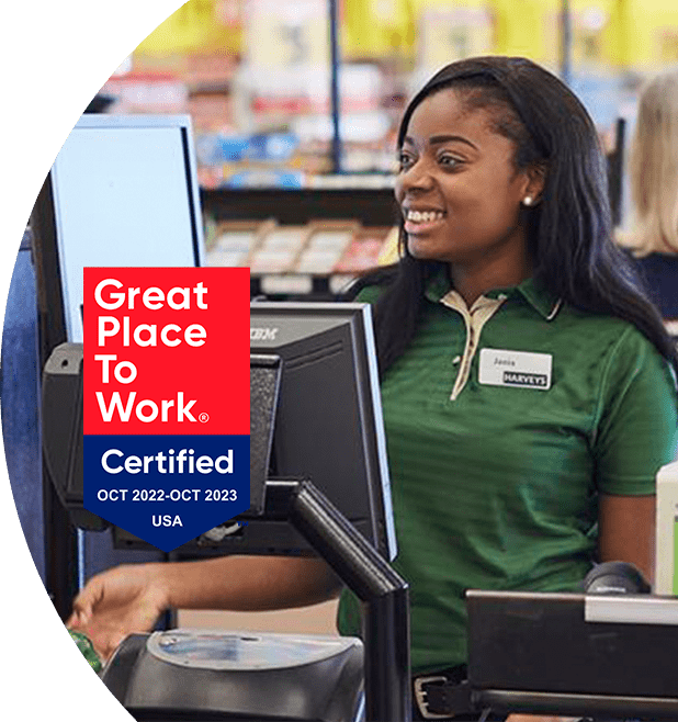 'Great Place to Work - Certified Oct 2022-Oct 2023' - Harveys Supermarket cashier smiling and checking out items