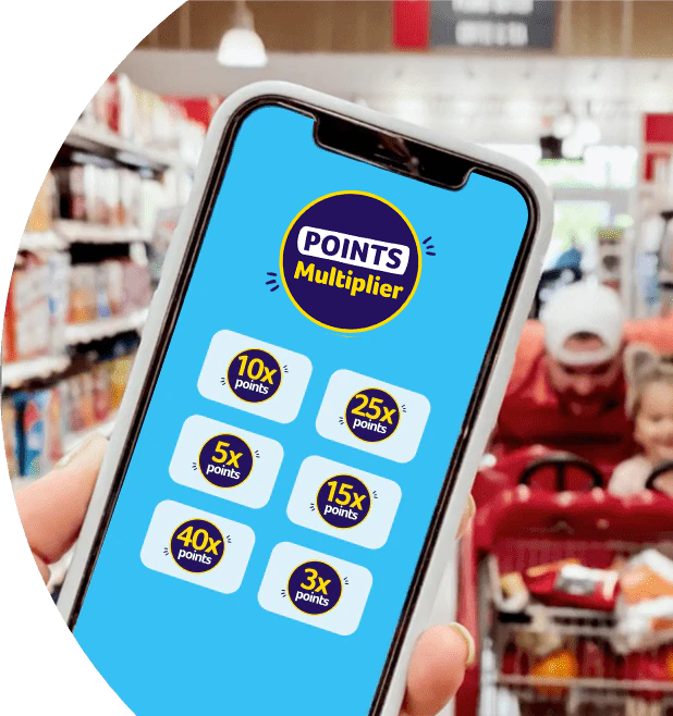 Foreground: Shopper holding a phone with the Points multiplier screen opened. Background: Man joyfully pushing a child in a shopping cart.