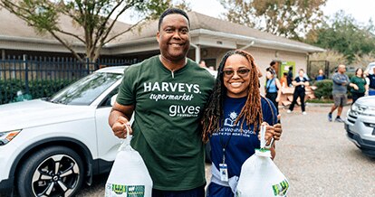 A male in a Harveys Supermarket shirt and female smiling holding food donations 
