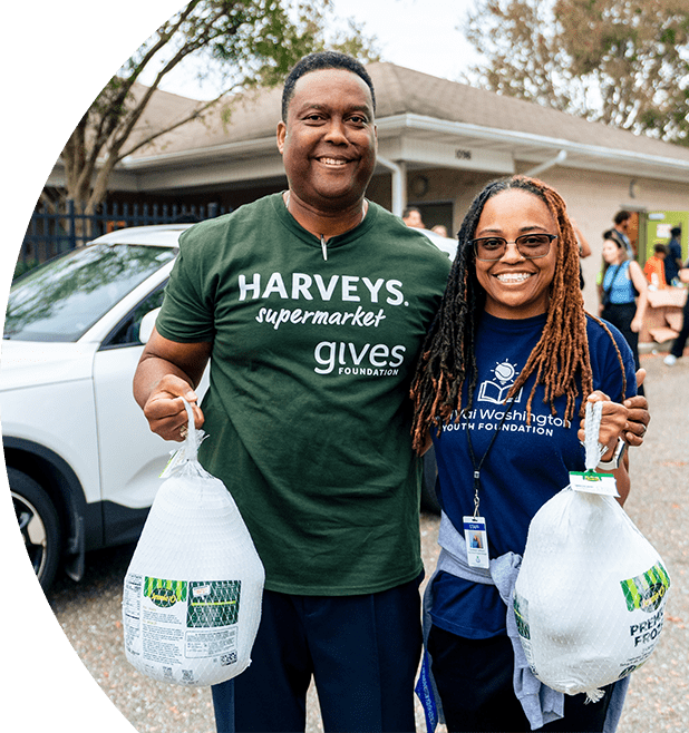 A male in a Harveys Supermarket shirt and female smiling holding food donations 