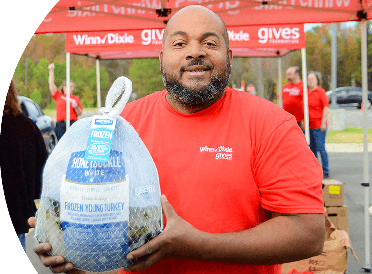 Man in a red Winn-Dixie gives shirt smiles while holding a turkey