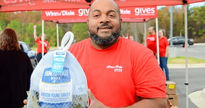Man in a red Winn-Dixie gives shirt smiles while holding a turkey