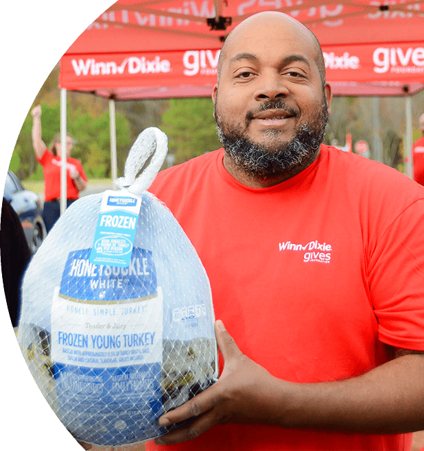 Man in a red Winn-Dixie gives shirt smiles while holding a turkey