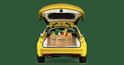 Bagged groceries inside the open trunk of a yellow car on a green background.