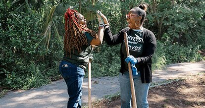 Harveys Supermarket Give Foundation volunteers joyfully high-five one another. They are working with gardening tools.