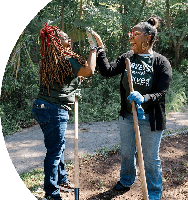Harveys Supermarket Give Foundation volunteers joyfully high-five one another. They are working with gardening tools.