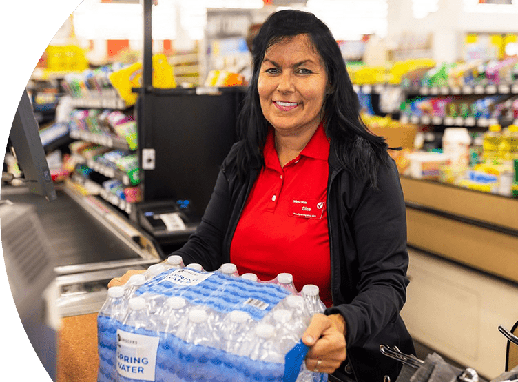 Smiling cashier checking out a pack of SE Grocers water bottles.