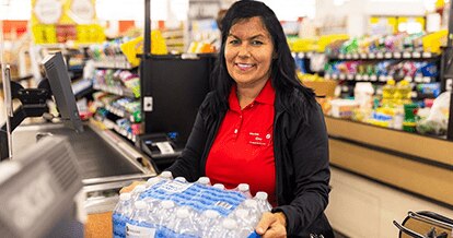 Smiling cashier checking out a pack of SE Grocers water bottles.