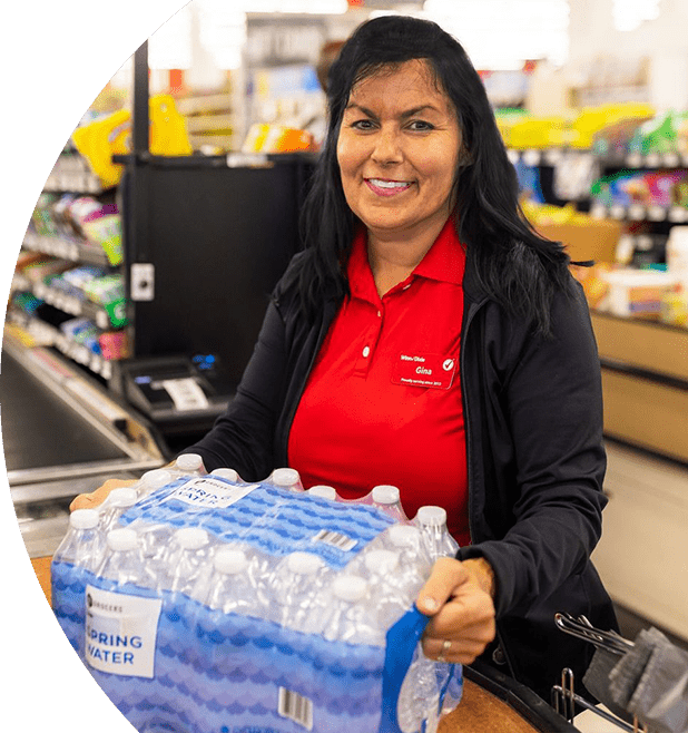 Smiling cashier checking out a pack of SE Grocers water bottles.