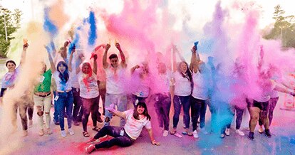 Group of people cheering and throwing colored powder in the air.