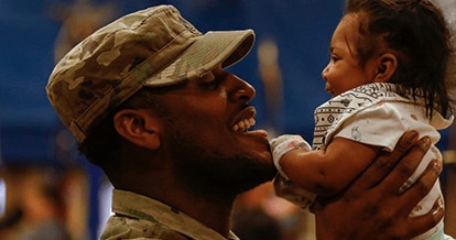 Smiling soldier in uniform picking up his baby.