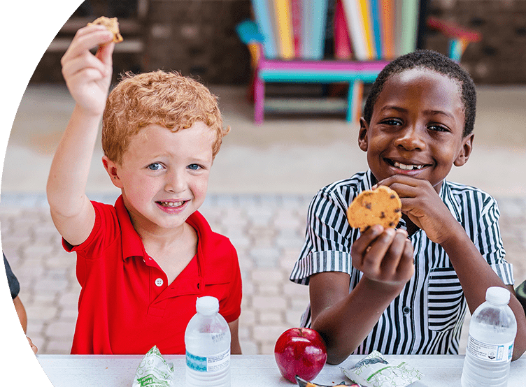 Two young boys eating a school lunch and smiling.