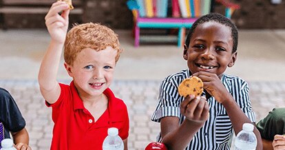 Two young boys eating a school lunch and smiling.
