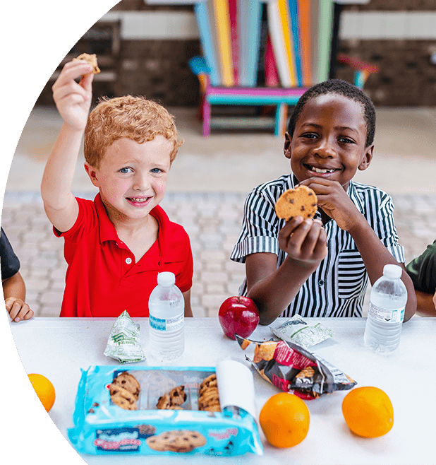 Two young boys eating a school lunch and smiling.