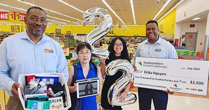 Four people smiling while one holds a big check.