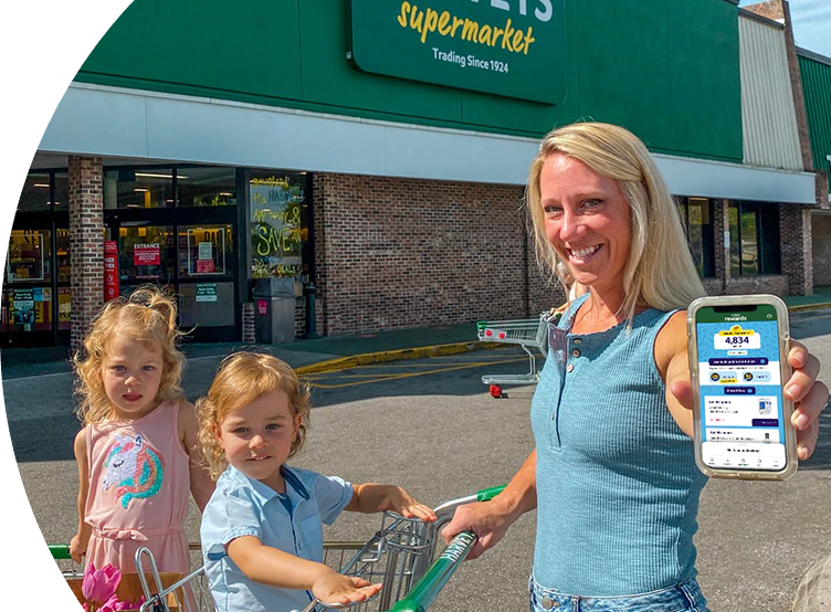Woman and her 2 kids outside of a Harveys Supermarket holding her phone.