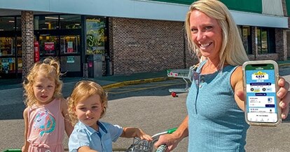 Woman and her 2 kids outside of a Harveys Supermarket holding her phone.