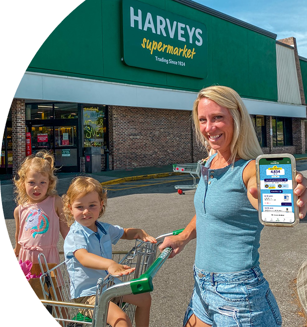 Woman and her 2 kids outside of a Harveys Supermarket holding her phone.