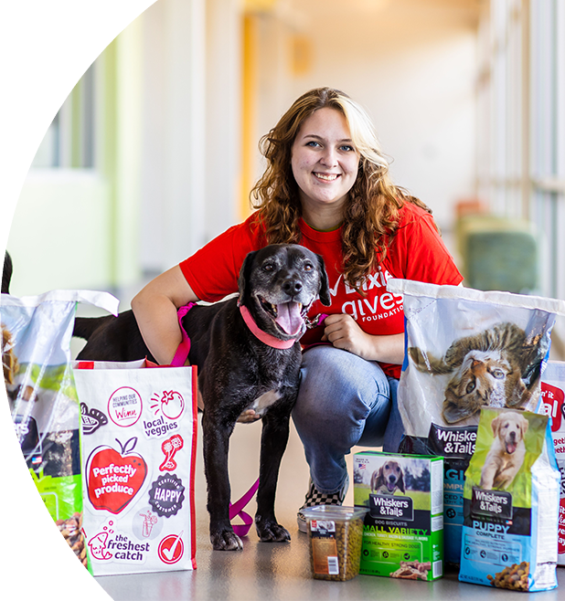 Pet food bags and Winn-Dixie re-usable bags set up in front of a woman kneeling and hugging a medium-sized dog. 